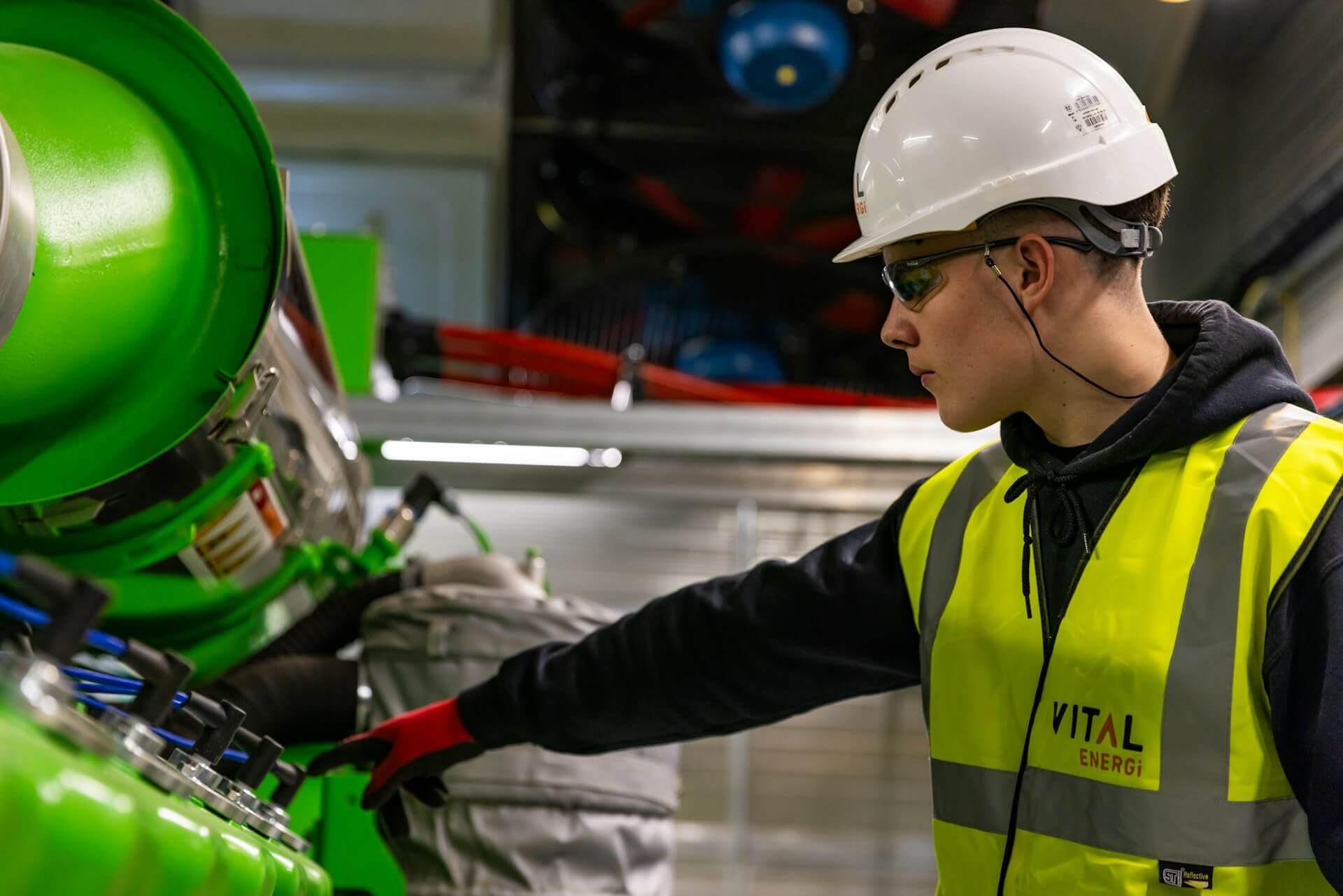 industrial maintenance engineer in a safety vest and hard hat inspecting a green pipe